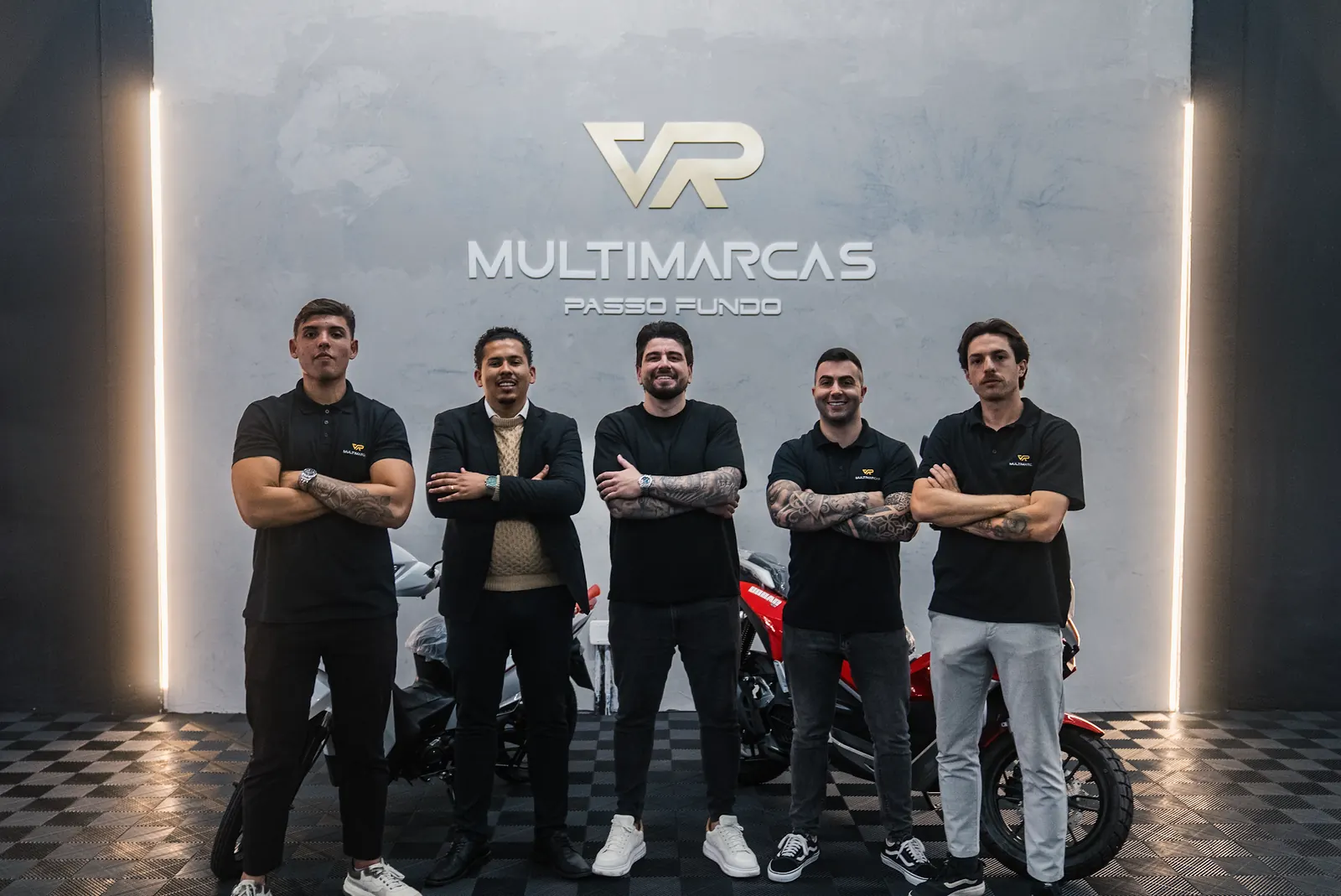 Equipe da VR Multimarcas Passo Fundo de braços cruzados na frente do logo, com motos atrás